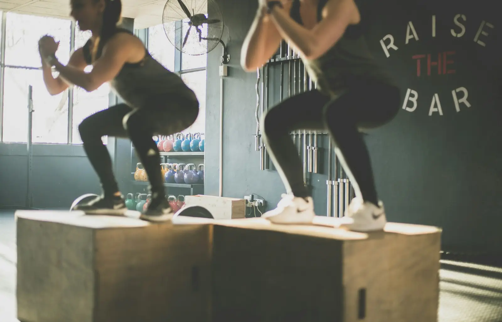 Due persone che si allenano con salti sui box nella zona funzionale, con kettlebell e bilancieri sullo sfondo